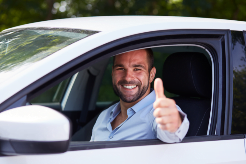 Man driving car and makes thumbs-up gesture