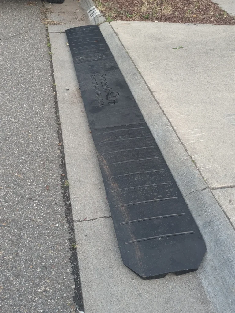 Close-up of connected Smooth Curb rubber ramp sections positioned beside a driveway curb